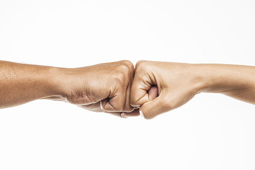 Two unrecognizable caucasian peoples fits are touching each other in front of white background. One hand belongs to a female person the other to a male.