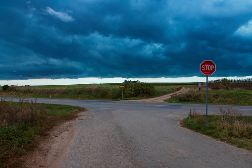 Crossroads on the road. The STOP road sign is visible. In the background is a dramatic sky with clouds.