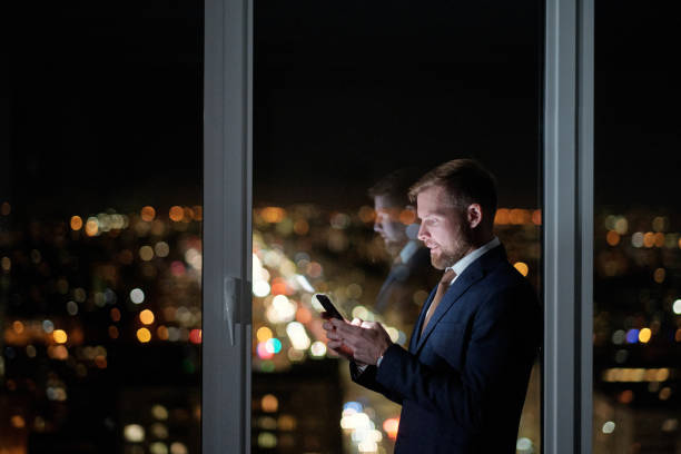 istock Side view of businessman scrolling in mobile phone against large window 1360841086