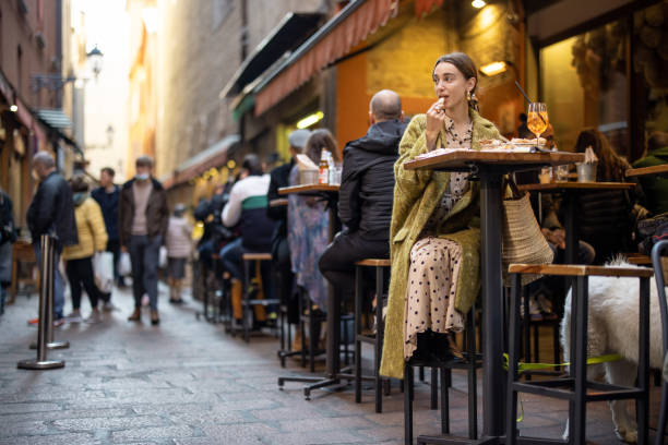 Woman sitting on crowded street at bar or restaurant outdoors Woman sitting on crowded street at bar or restaurant outdoors in Bologna city. Concept of Italian lifestyle and gastronomy busy restaurant tables stock pictures, royalty-free photos & images