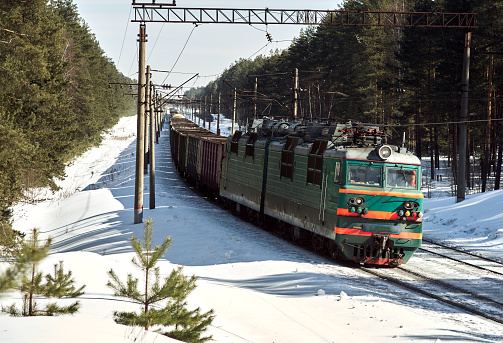 The locomotive transports freight cars in winter through the forest