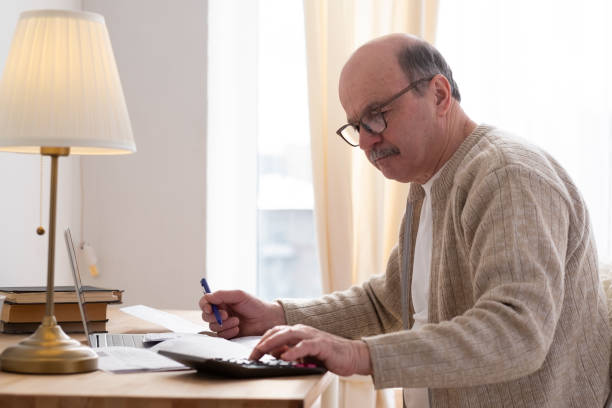 istock Senior man sitting with paperwork and using calculator while counting money 1360848418