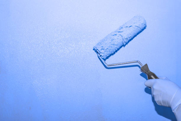 istock Painting works. A woman paints the wall with a roller with lilac paint, copy space on the left. The color of the trend of the year 1360852257