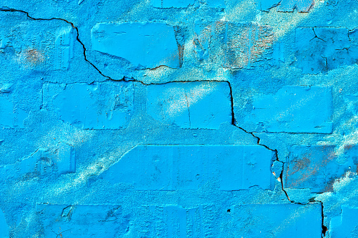 Cracked blue brick wall background. Worn damaged house facade surface.