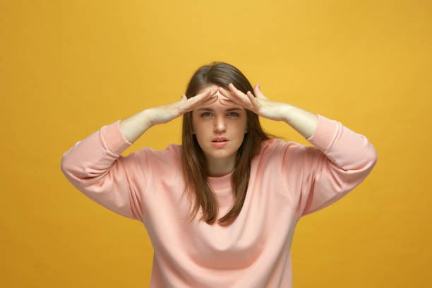 istock Attentive young girl holding hands at forehead looking at camera on yellow studio background. Searching, expectations 1360855927