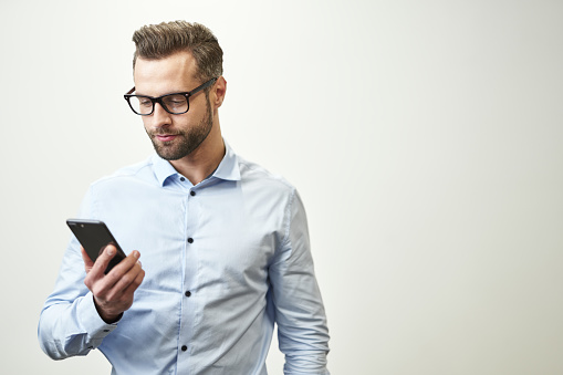 Calm handsome man wearing spectacles looking at the screen of a smartphone. Template banner on white background