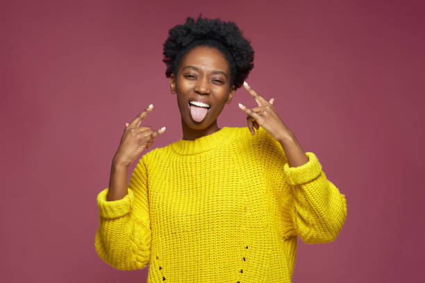 Horns rock and roll gesture. Happy cool audacious african american young woman sticking tongue, show rock-n-roll sign Horns rock and roll gesture. Happy cool modern audacious african american young woman sticking tongue, show rock-n-roll sign. High quality photo horn sign stock pictures, royalty-free photos & images