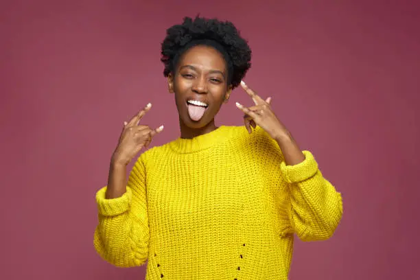 Photo of Horns rock and roll gesture. Happy cool audacious african american young woman sticking tongue, show rock-n-roll sign