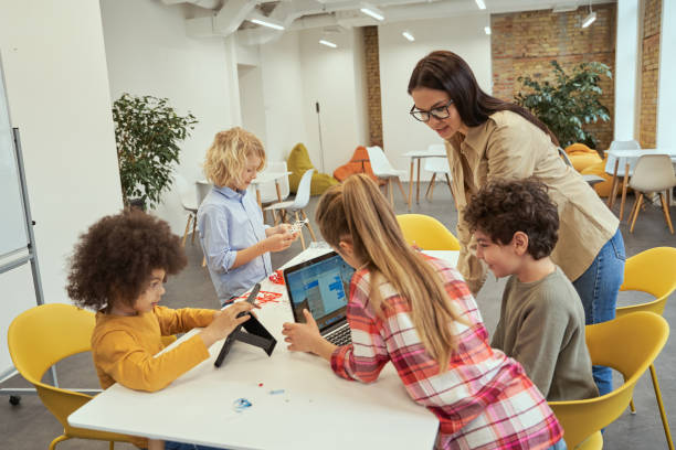 istock Fun and engaging. Happy children using gadgets during STEM class with young female teacher 1360857697