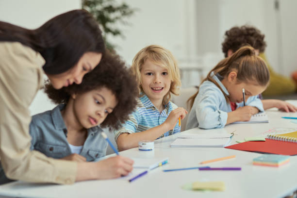 istock Making progress. Smiling little schoolboy looking at camera while sitting at the table in elementary school classroom together with other kids 1360857702