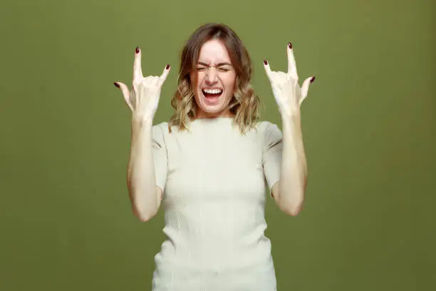 Exited cool young girl show rock n roll gesture by raised hands, screaming. Female rocker music fan showing horns sign by fingers, yelling closed eyes feel delight. High quality photo