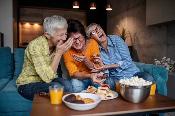 Three senior women having wonderfull time while eating sweet and salty snacks in the living room stock photo