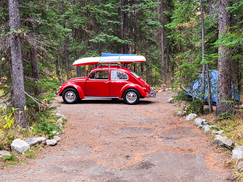 Classic 70s Volkswagen Beetle parked in forest Campground.  Well maintained camp site equipped with tent and a Kayak on roof rack ready to explore the local Saskatchewan river.