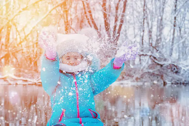 Child at winter. Happy girl outdoors.Funny little girl having fun in beautiful winter park.Child playing with snow in winter. Little girl in catching snowflakes in winter park on Christmas.