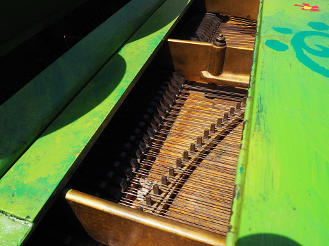 Strings, soundboard and piano mechanics. Piano on the street. Piano painted green. Performance of a piece of music. Street concert on a summer sunny day