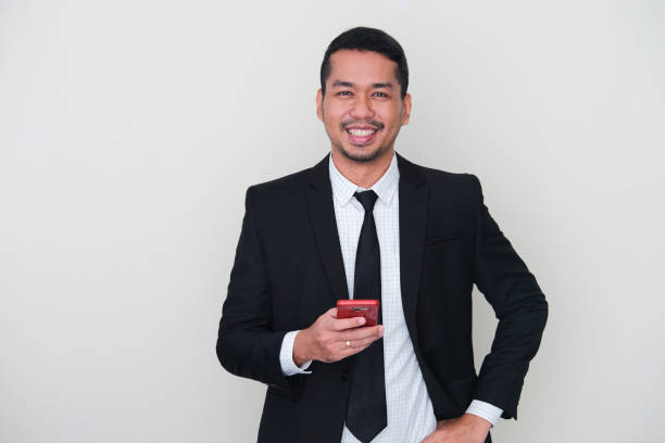 黒いスーツを着て、携帯電話を使用しながら笑顔を結ぶ大人のアジア人男性 - asian ethnicity suit business men ストックフォトと画像