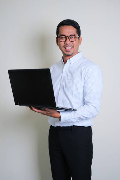 istock Young Asian business man holding laptop computer while smiling confident 1360885683