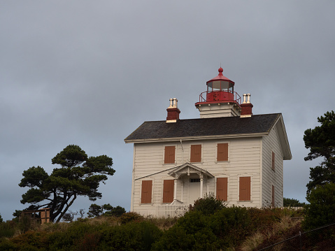 Two story white wooden Yaquina Bay lighthouse with shuttered windows and red metal frame over the lighthouse beacon.