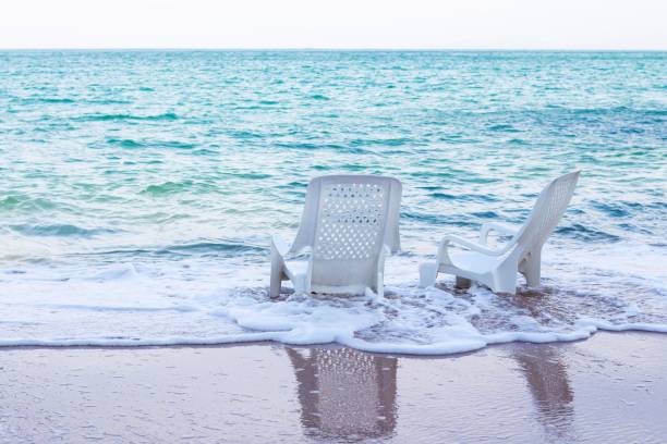 Empty white plastic chairs on the beach with beautiful white ocean waves. stock photo