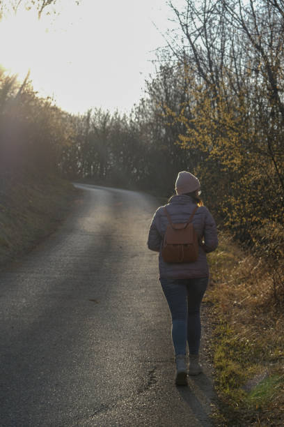 istock Woman walking alone on the road thru the forest 1360921755