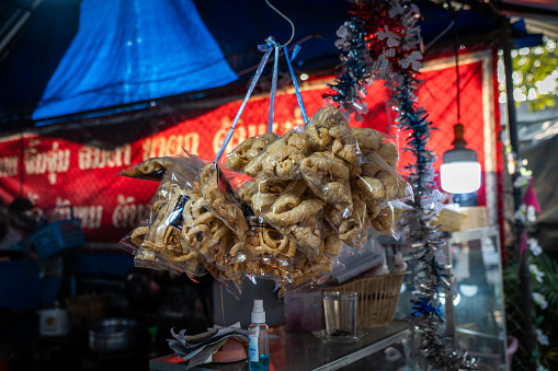 Bagged pork rinds (pork skin) for sale at an outdoor market with street food vendors at a residential neighborhood in Bangkok, Thailand.