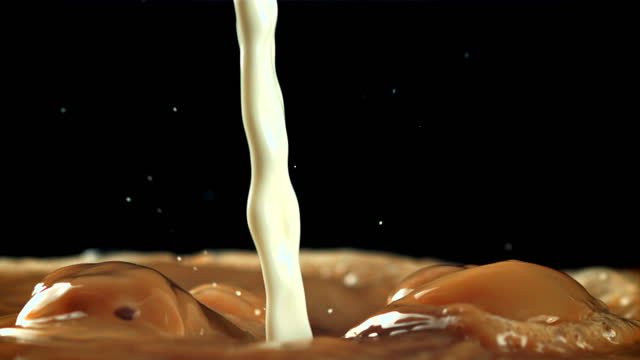 Milk is poured into coffee with splashes. Filmed is slow motion 1000 frames per second.
