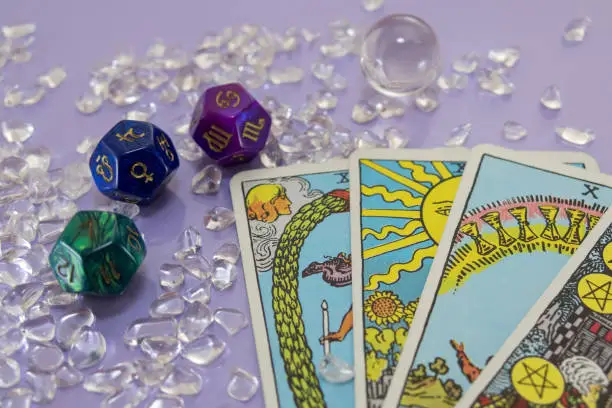 Tarot card, Scattered astrology dice, scattered crystal pebbles on a light purple background