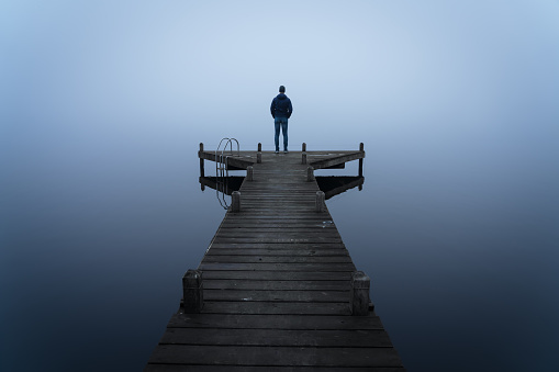 Depressed emotions concept: a man standing at the end of a jetty, on a foggy, autumn day.