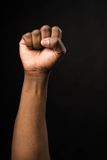 Raised fist of a black man, on black background.