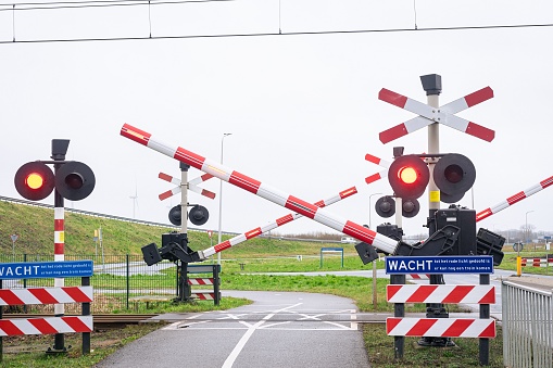 Level crossing with closing railway trees and flashing warning lights. Dutch text on the blue signs means: Wait until the red light is off, another train may come.