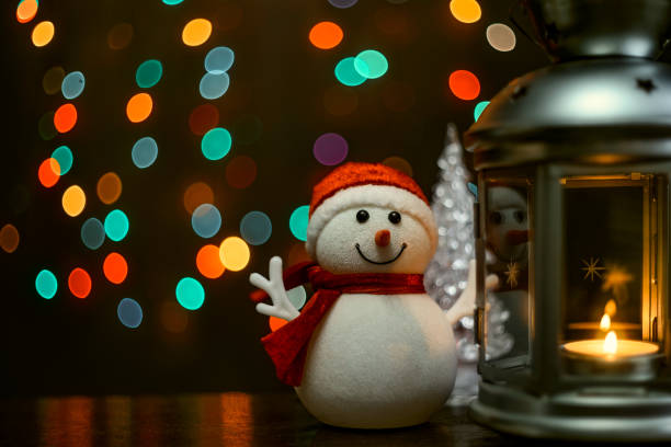 istock Christmas card: a snowman, a lantern with candles and blurry lights in the background. 1360928690