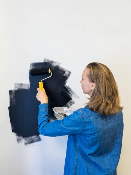 istock Woman painting a wall in black. Copy space. Vertical view. 1360929933