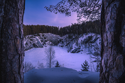 view of a frozen mountain lake covered with snow and surrounded by rocky cliffs on a winter evening