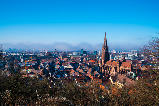 Germany, Freiburg im Breisgau cityscape, ancient gothic muenster cathedral in winter with foggy atmosphere, panorama view above at sunset