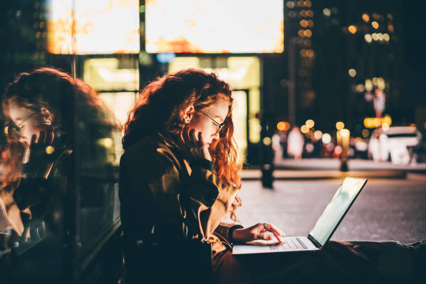 Woman using laptop on night city street. stock photo