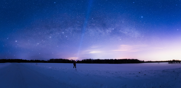 Milky Way Arc and sky full of stars above the snow field and a man with flashlight pointing in the sky