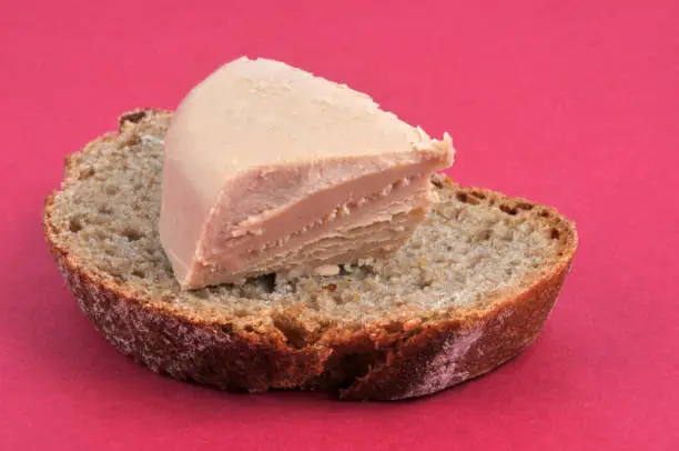 Piece of foie gras on a bread spread in close-up on a red background