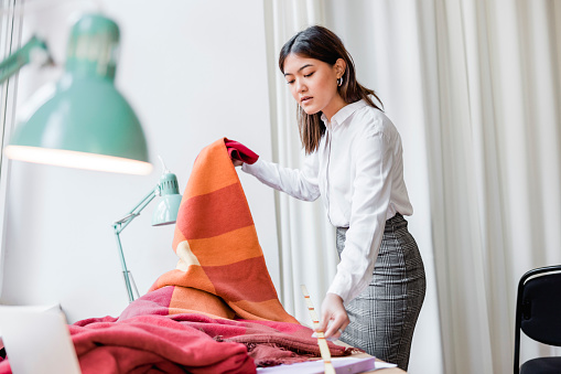 Female interior designer working in her studio. Woman measuring a fabric with in her workshop.