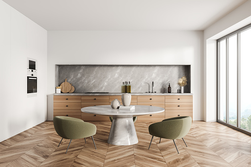 White minimalist kitchen interior with grey marble materials, two green armchairs, wooden drawers, round table and parquet floor. Concept of modern house design. 3d rendering