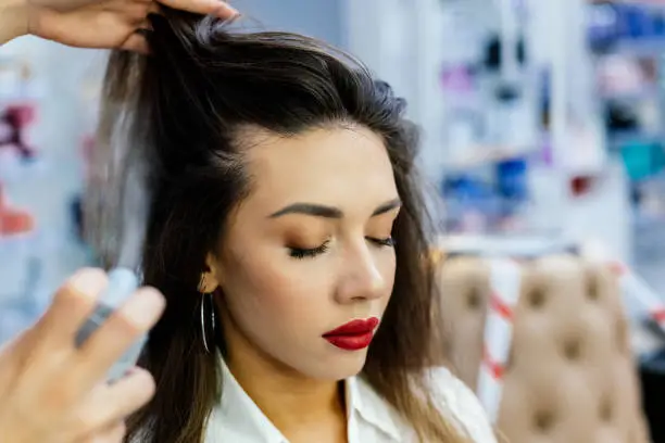 A beautiful brunette woman is sprayed on her hair in a beauty salon.