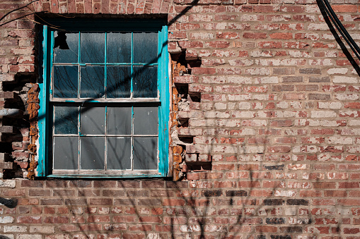 Colorful window with broken pane set in damaged brick wall with negative space for copy