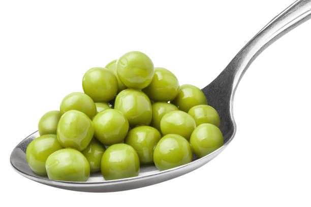 A stack of table spoons holding several green peas