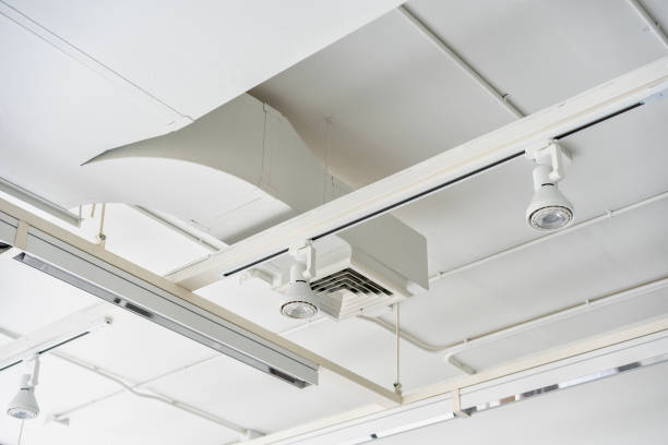 istock Ceiling mounted cassette type air condition units with other parts of ventilation system (tubes, cables and vents) located inside commercial hall with hanging lights and other construction parts. 1361032751