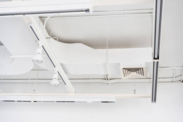 istock Ceiling mounted cassette type air condition units with other parts of ventilation system (tubes, cables and vents) located inside commercial hall with hanging lights and other construction parts. 1361032771