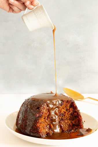 Hand pouring Toffee sauce over Sticky Toffee Pudding. Typical British dessert