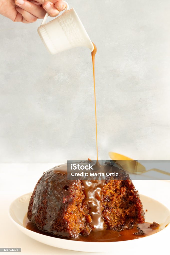 Sticky Toffee Pudding Hand pouring Toffee sauce over Sticky Toffee Pudding. Typical British dessert Mousse - Dessert Stock Photo