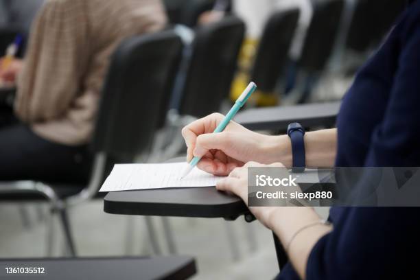 A Girl Writes A Dictation Or Fills Out Documents In The Audience Sitting On A School Chair With A Writing Stand Closeup Stock Photo - Download Image Now