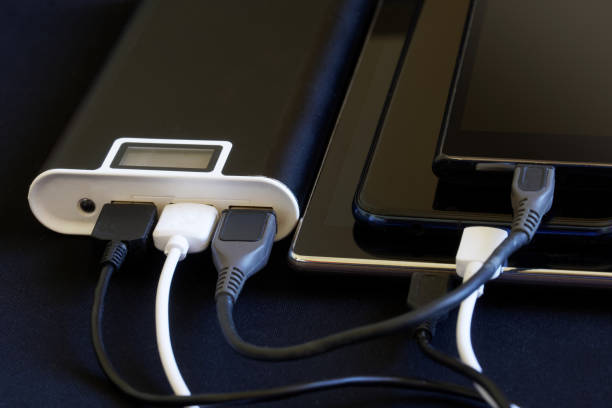 One external battery - powerbank charges three gadgets at once: two smartphones and a tablet. Dark background. The concept of recharging a variety of smart devices