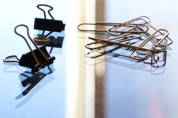 Photo of A pile of metal paper clips on a reflective glass surface. Office work concept. Macro. Selective focusing