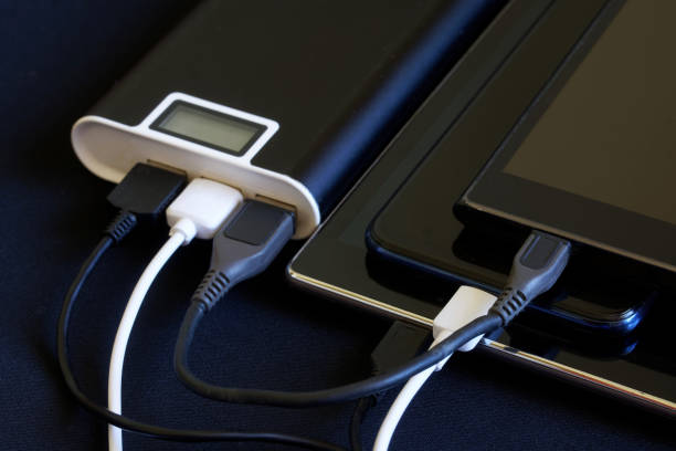 istock Three USB gadgets - two smartphones and a tablet are charged from one external battery - powerbank. Dark background. The concept of recharging a variety of smart devices 1361035535